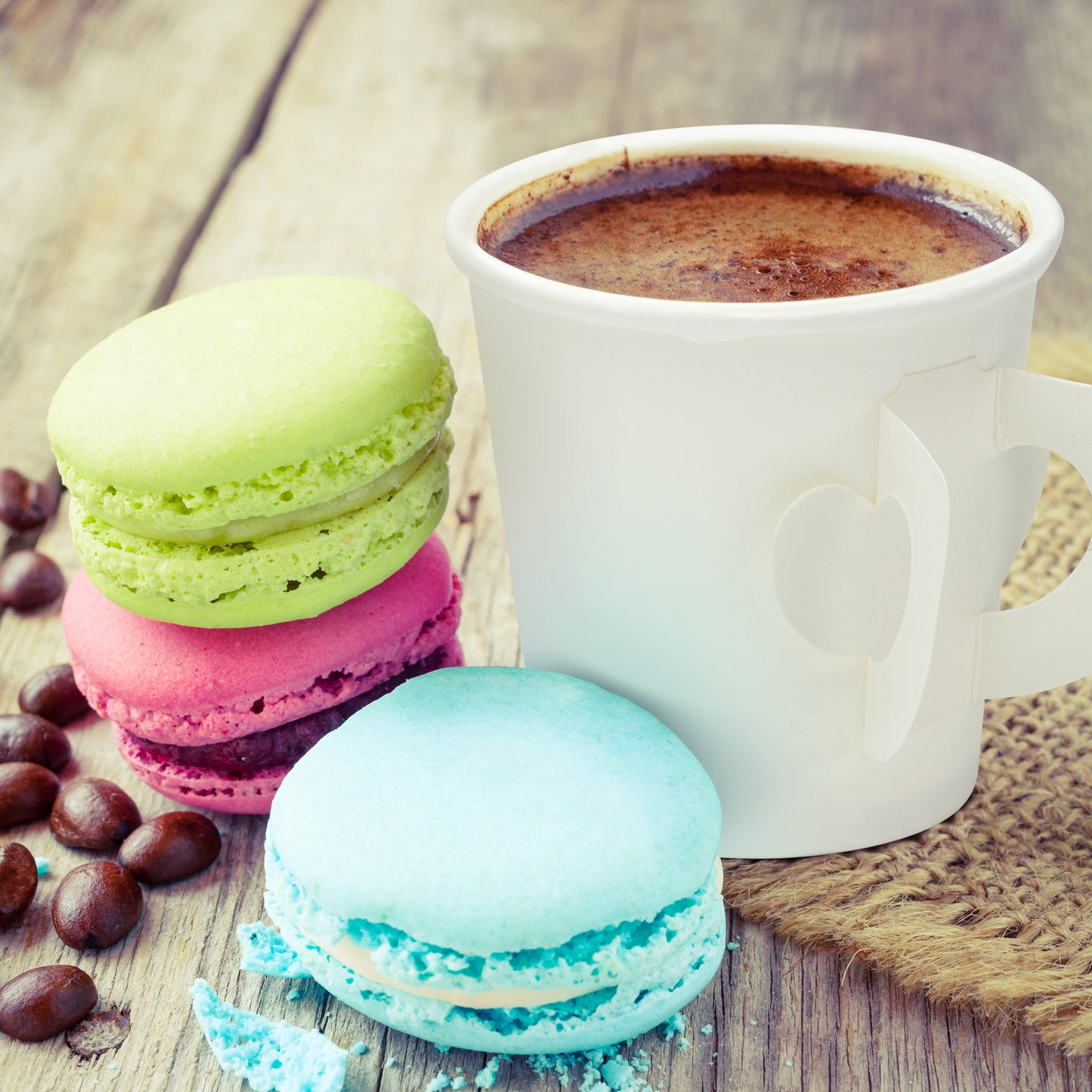 Colorful macarons with a white mug of coffee on a wooden surface
