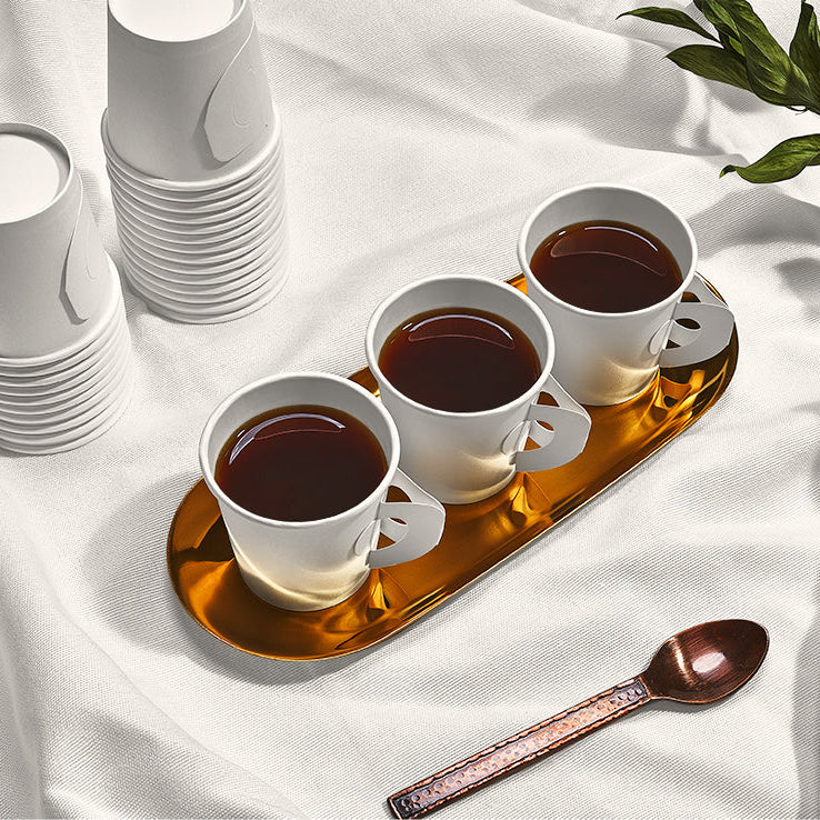 Four white cups with dark liquid on a gold tray, surrounded by stacked white cups